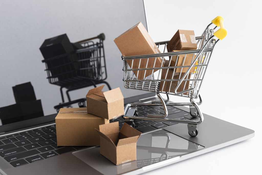 carinho de compra e caixa sobre um teclado de notebook. A imagem representa a industria de consumo.